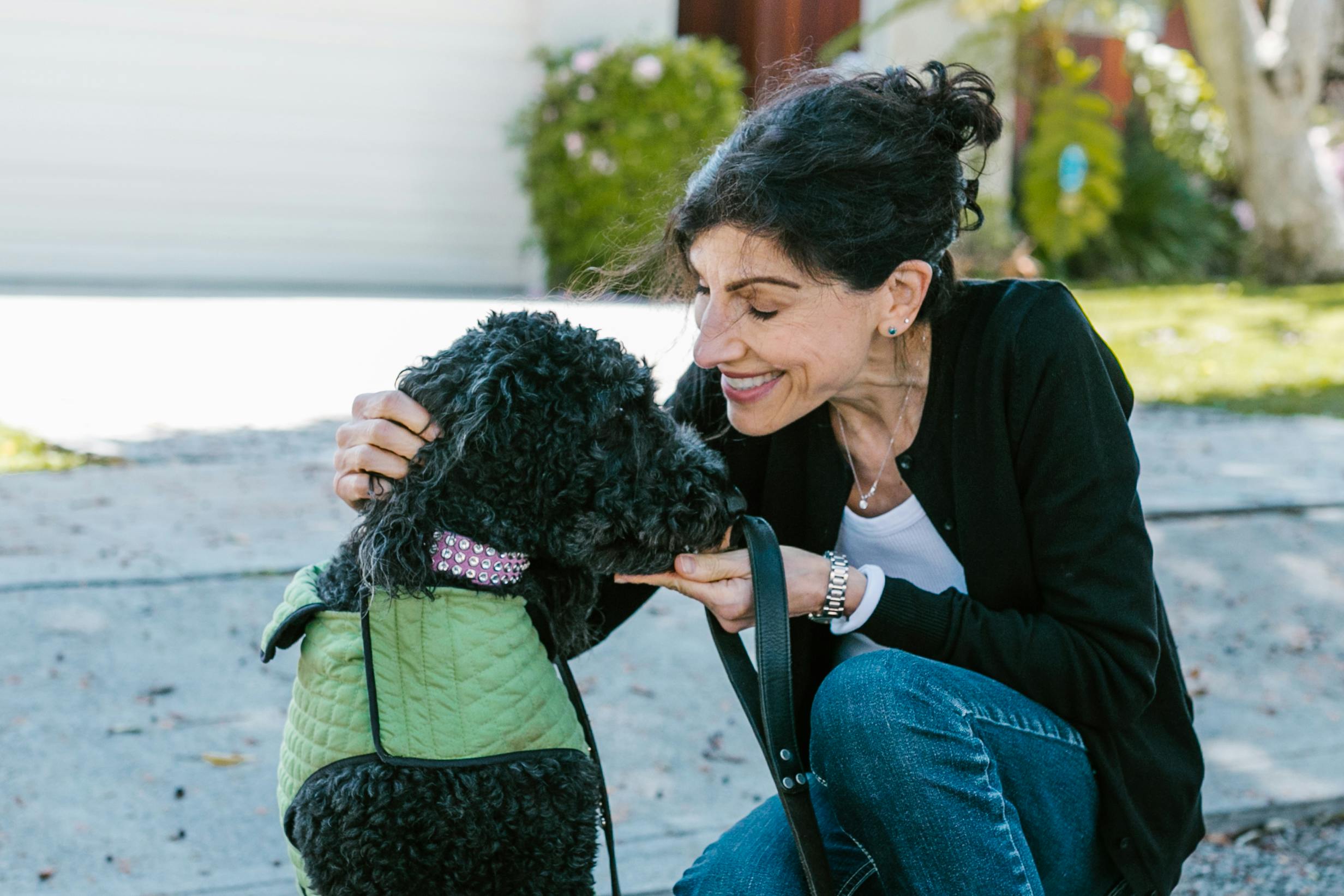 A woman happily interacts with her poodle dog outdoors, showcasing a warm bond.